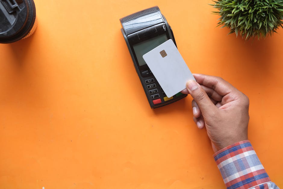 A stressed man looks at his smartphone, holding a credit card in his hand.